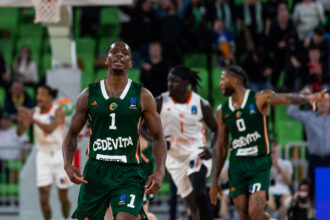 Basketball player in a green jersey number 1 runs toward the camera during a game with a cheering crowd in green seats behind him.