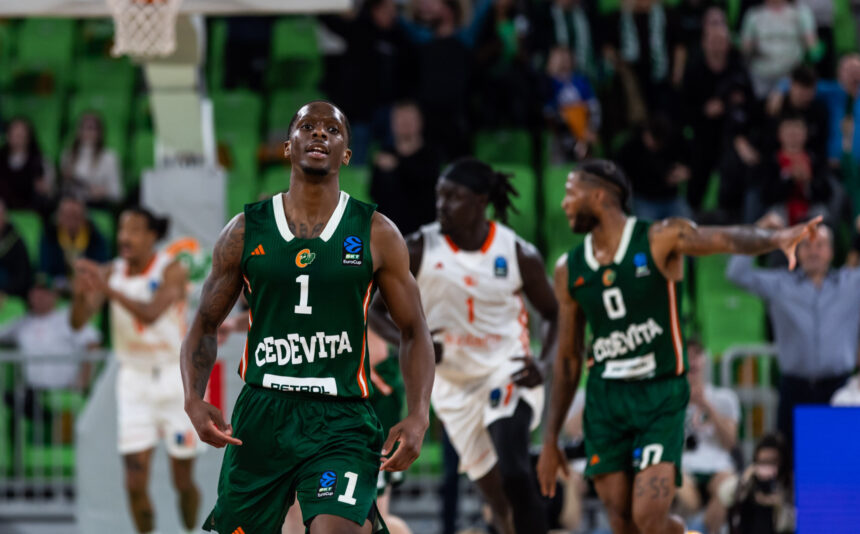 Basketball player in a green jersey number 1 runs toward the camera during a game with a cheering crowd in green seats behind him.