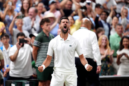 A man in a white polo shouts with clenched fists as a crowd applauds behind him at a sporting event