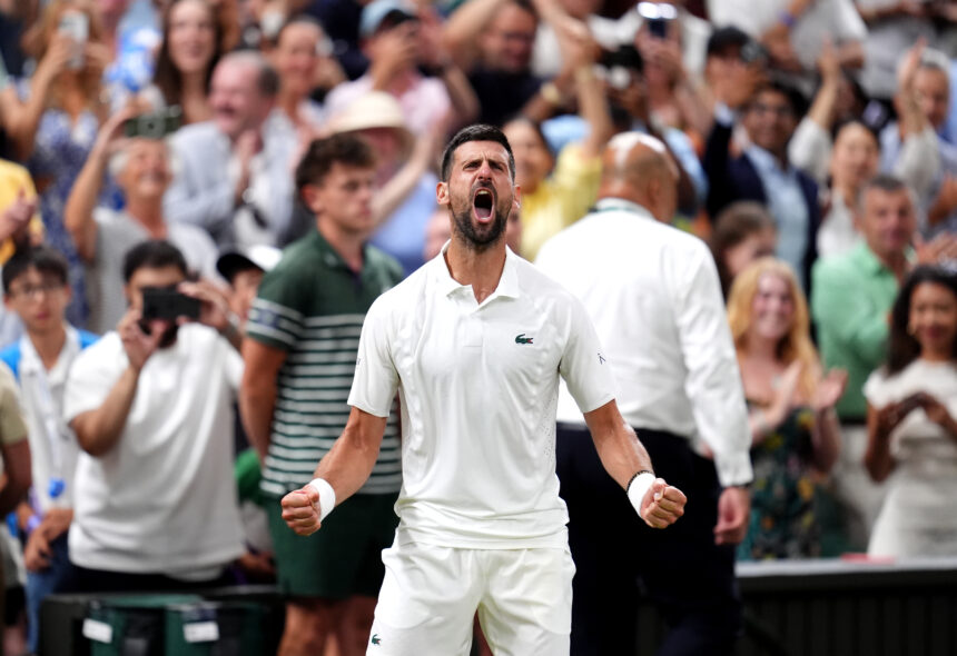 A man in a white polo shouts with clenched fists as a crowd applauds behind him at a sporting event