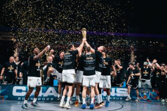 Basketball players lift a championship trophy on the court as gold confetti falls around them.