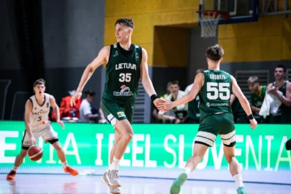 Lithuanian basketball player wearing number 35 in green jersey extends hand to teammate on a lit indoor court during a game.
