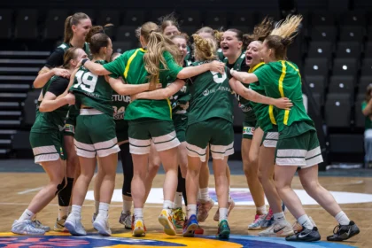 Women’s volleyball team huddles in green uniforms, arms around each other in celebration on the court.
