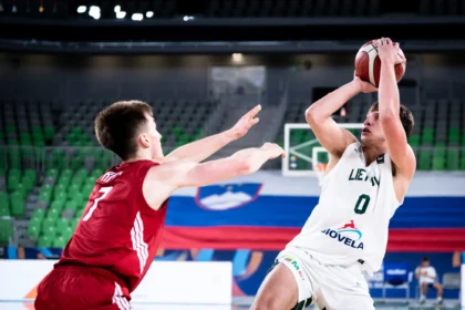 Basketball player in white drives toward the hoop while defended by a red-team defender nearby