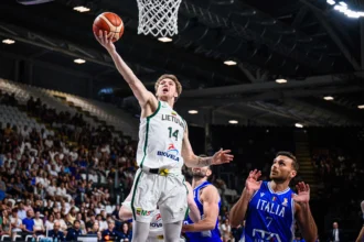 Lithuanian player in white jersey leaps toward basket for score against Italy in an arena with cheering crowd behind.