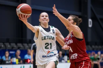 Two female players clash for the ball during a basketball game; one in a white Lithuania jersey reaches up for the ball while a defender in red guards.