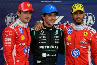 Three Formula 1 drivers pose on a podium: left and right wear red Ferrari suits, center in a black Mercedes Petronas suit with arms around each other; backdrop shows sponsor logos and 'United Against Online Abuse' text.