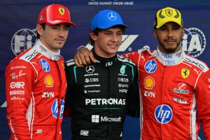 Three Formula 1 drivers pose on a podium: left and right wear red Ferrari suits, center in a black Mercedes Petronas suit with arms around each other; backdrop shows sponsor logos and 'United Against Online Abuse' text.