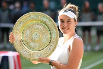 Smiling female tennis player holding a large ornate gold trophy plate at an outdoor match.