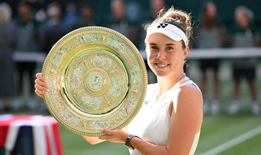 Smiling female tennis player holding a large ornate gold trophy plate at an outdoor match.