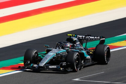 Silver Mercedes Formula 1 car on a dark track with bright red, yellow, and green curbs in the background.