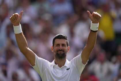 Athlete with white shirt and wristbands raising both arms in victory on a crowded tennis court.