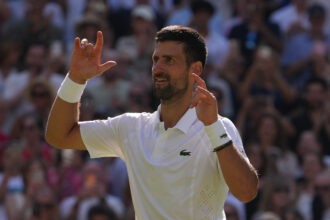Tennis player in a white shirt celebrates with raised arms as a cheering crowd looks on in the background.
