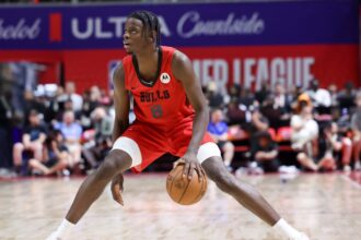 Basketball player in a red Bulls jersey dribbling the ball on a court with a crowd in the background