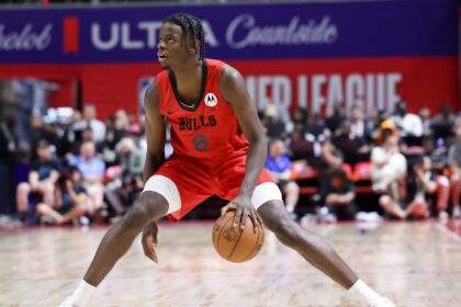 Basketball player in a red Bulls jersey dribbling the ball on a court with a crowd in the background