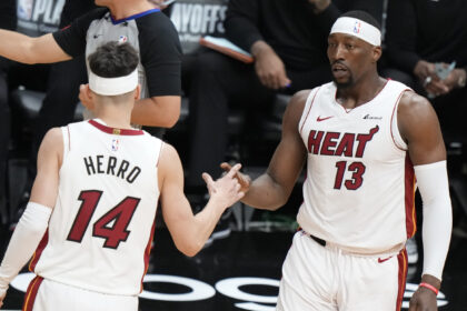 Miami Heat players high-fiving on a basketball court during a game; jersey numbers 14 and 13 visible, one with 'HERRO' on the back.