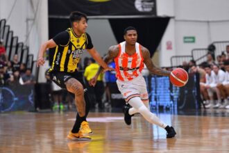 Two basketball players chase the ball on court; one in yellow-and-black defends a white-and-orange jersey player who is dribbling.