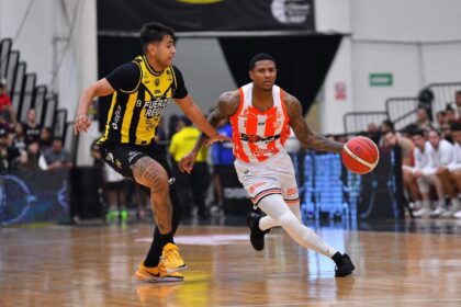 Two basketball players chase the ball on court; one in yellow-and-black defends a white-and-orange jersey player who is dribbling.