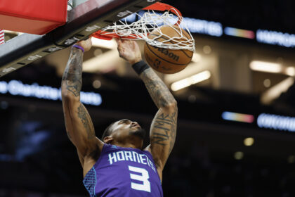 Basketball player in a purple Hornets jersey dunks the ball through the hoop during a game, tattoos visible on arms.