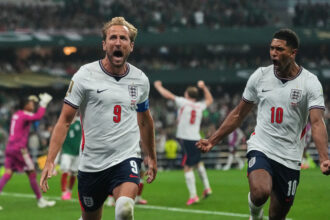 England footballers celebrate a goal, front two players wearing number 9 and number 10 jerseys on the pitch.