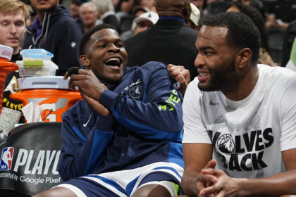 Two basketball players sit side by side, one laughing with mouth open, the other smiling, during a playoff event of an NBA game.