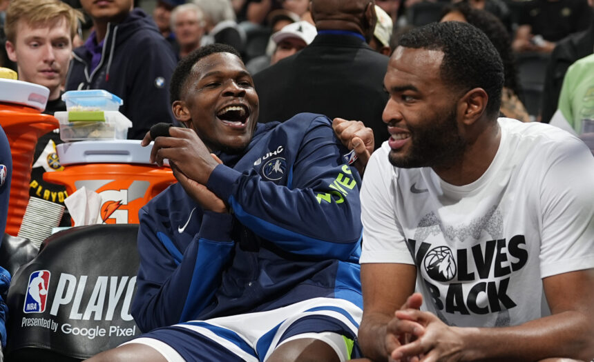 Two basketball players sit side by side, one laughing with mouth open, the other smiling, during a playoff event of an NBA game.