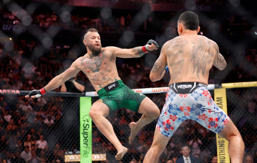 Two male UFC fighters collide in the octagon as the left fighter throws a punch toward his tattooed opponent amidst a crowded arena.