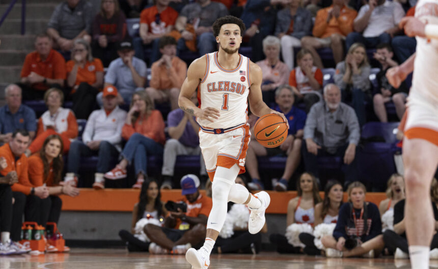 Clemson basketball player (number 1) dribbling down the court with a crowded arena in orange jerseys behind him.