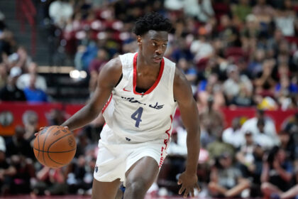 Basketball player in white jersey dribbles down court with a crowd in the stands behind him.